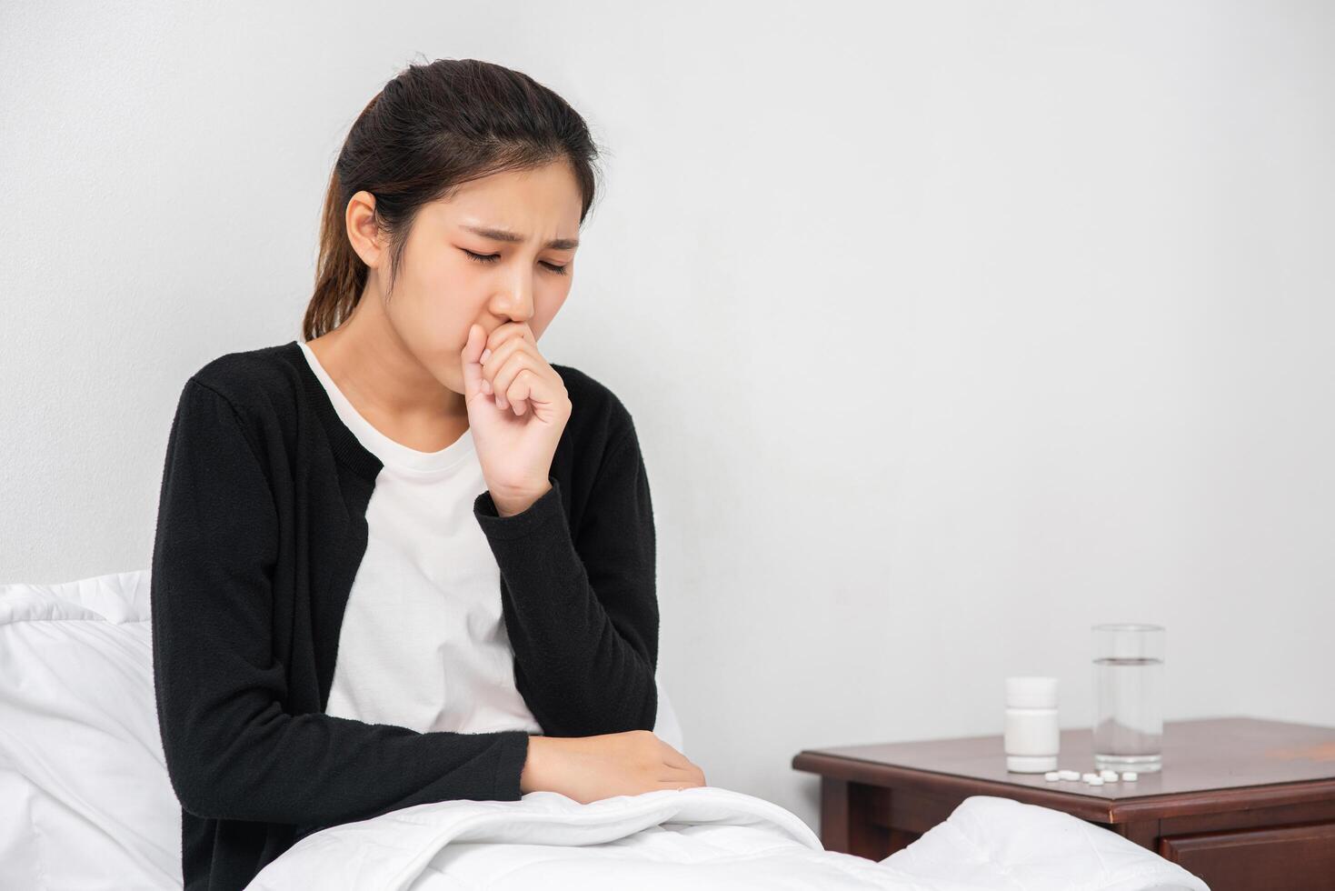 The woman coughed and covered her mouth with her hand and sat on the bed. photo