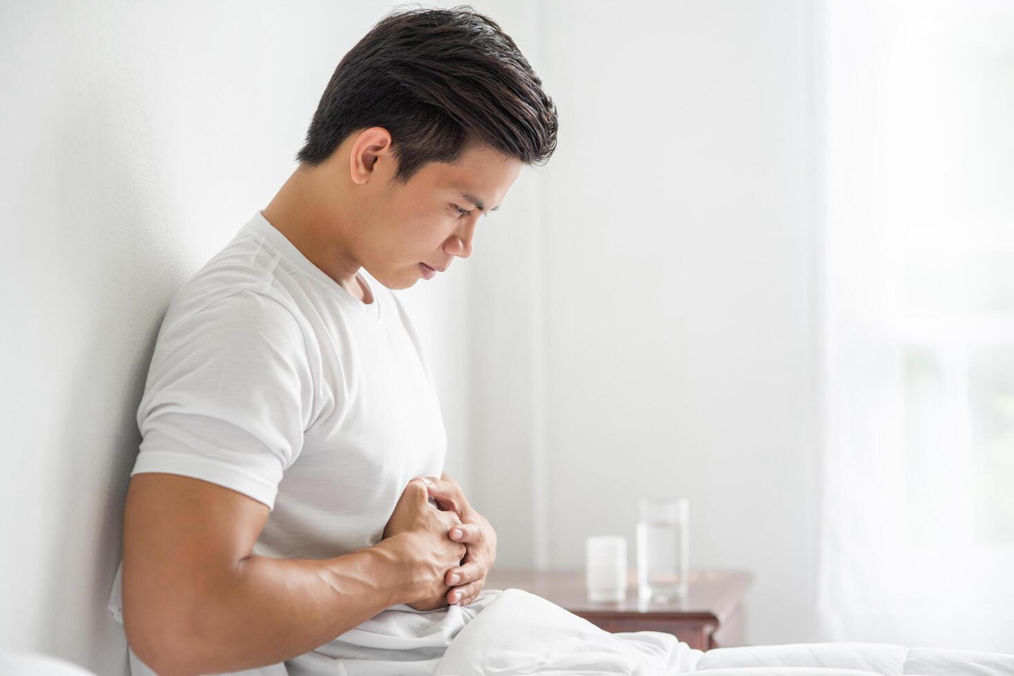 A man sits in bed with a stomachache and presses his stomach with his hands. photo