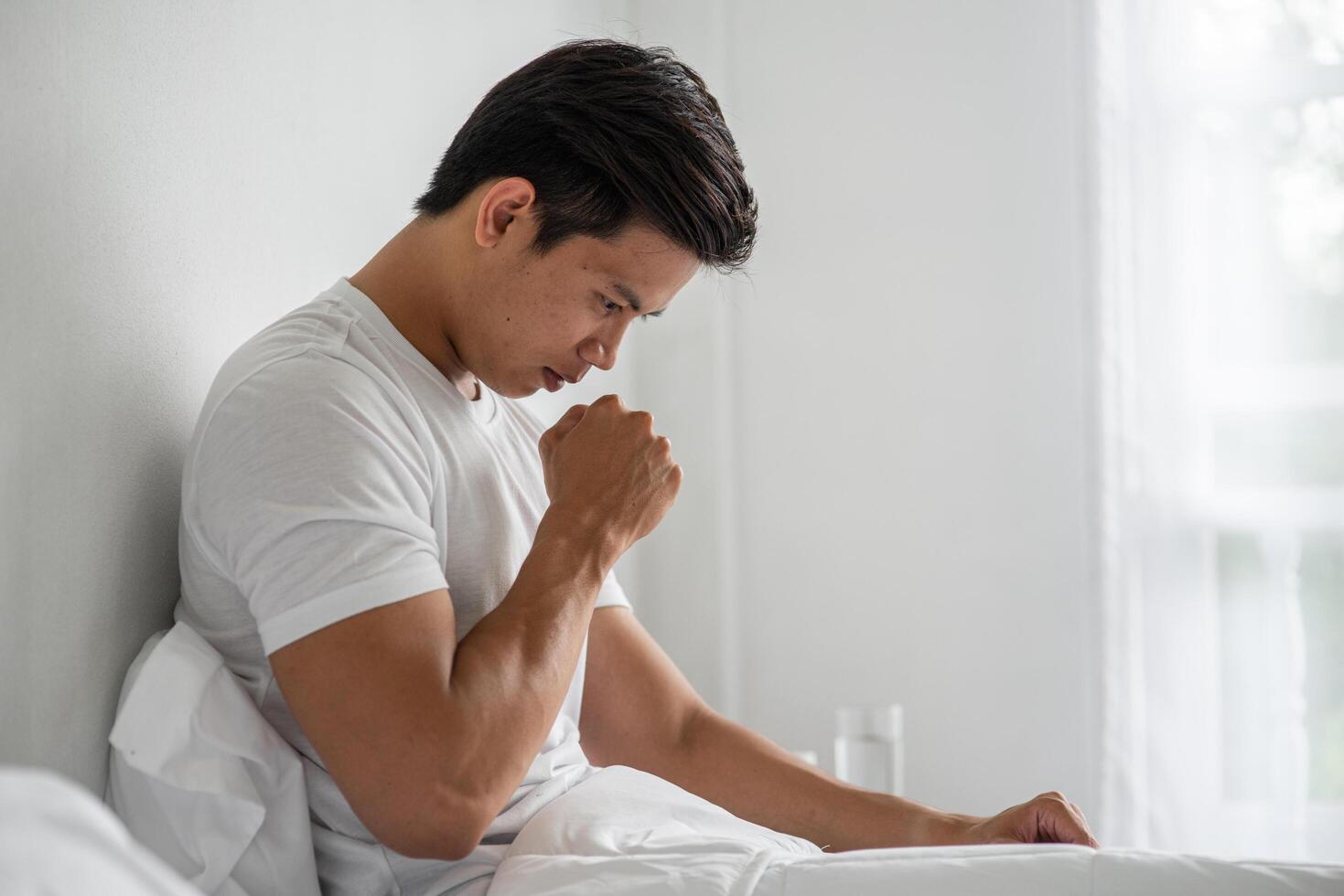 The man coughed and put his hand over his mouth and sat down on the bed. photo