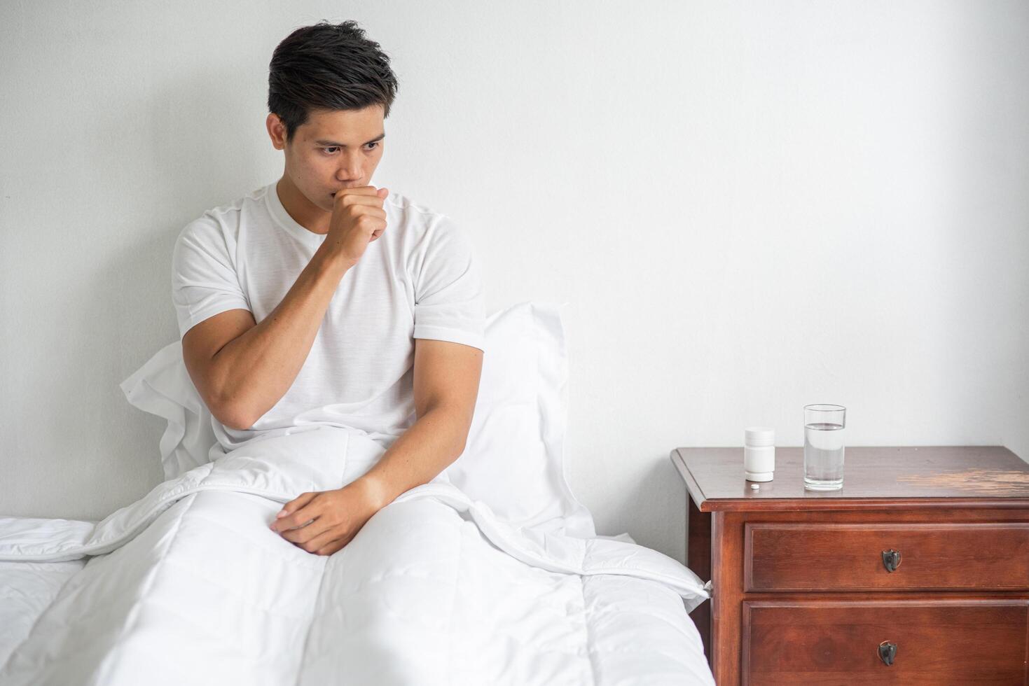 The man coughed and put his hand over his mouth and sat down on the bed. photo