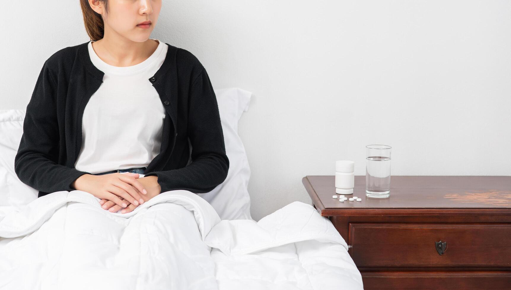 una mujer incómoda se sienta en la cama y tiene un medicamento sobre la mesa. foto