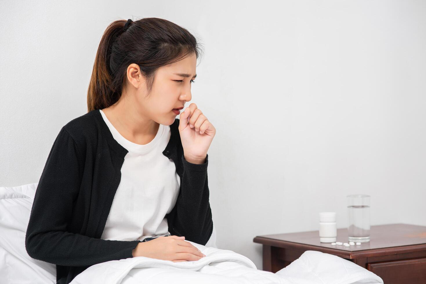 The woman coughed and covered her mouth with her hand and sat on the bed. photo