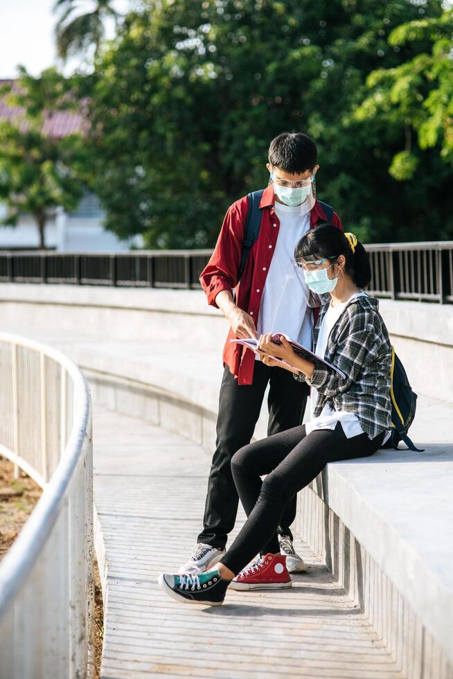 Male and female students wearing masks sit and read books on the stairs ...