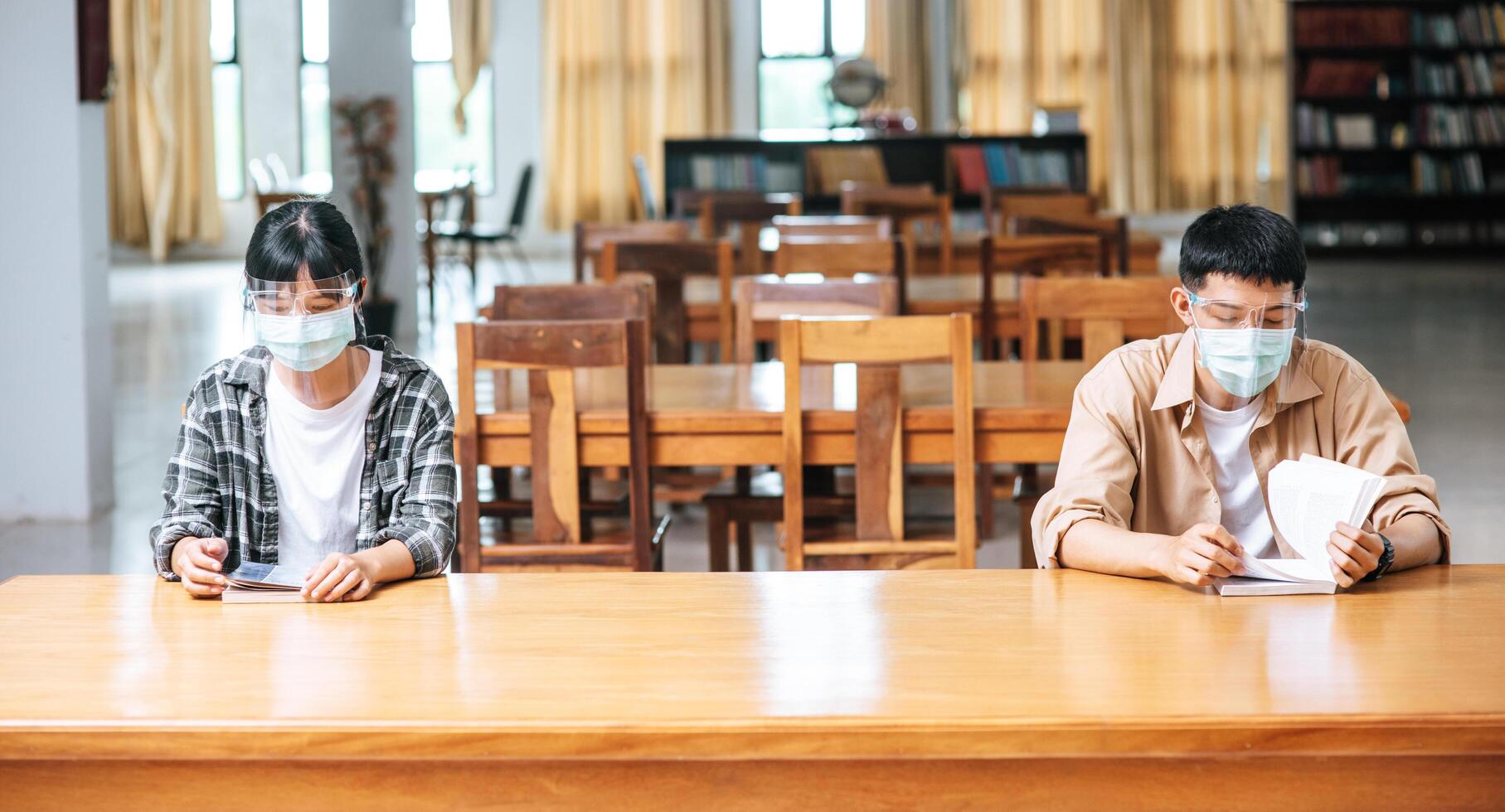 hombres y mujeres con máscaras se sientan y leen en la biblioteca. foto