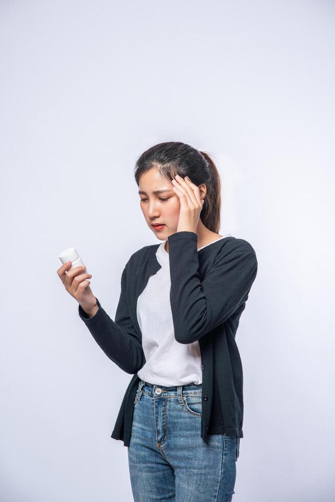 A woman with pain in her hand holds a medicine bottle and the other hand but on her head photo