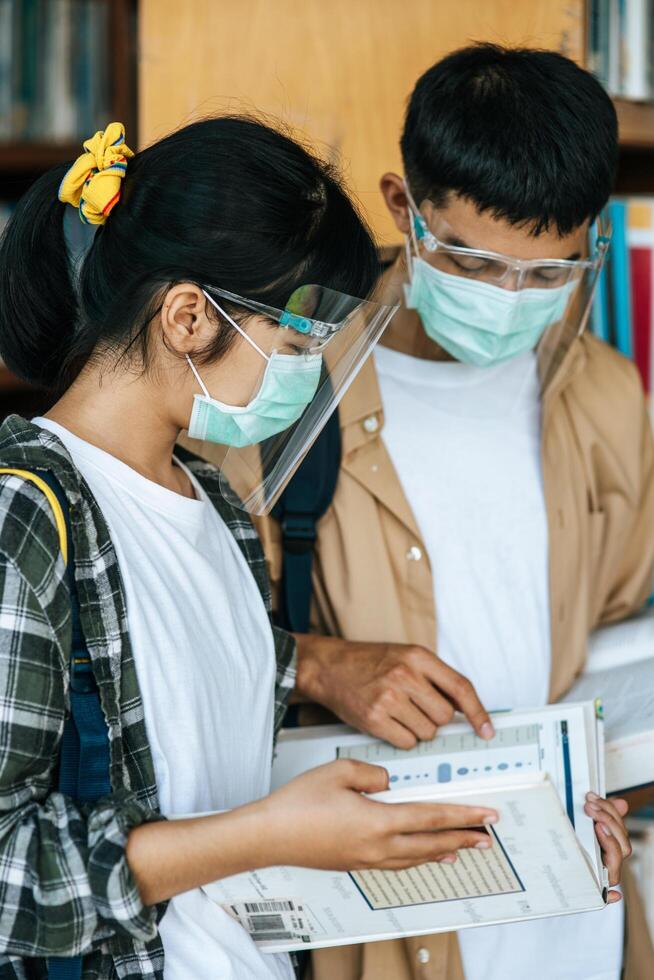 hombres y mujeres con máscaras se paran y leen en la biblioteca. foto