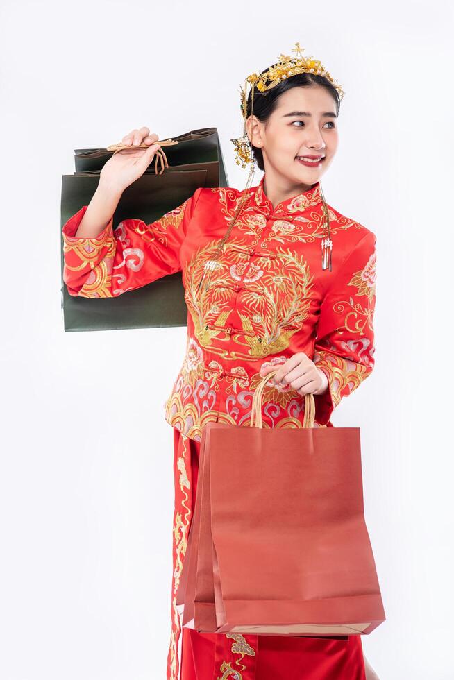 Mujer vistiendo traje cheongsam sonrisa con bolsa de papel de compras en año nuevo chino foto