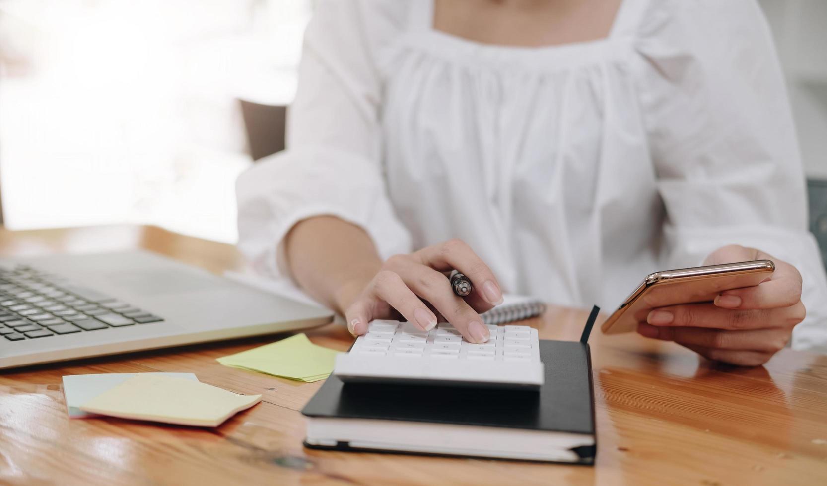 woman using smartphone, calculating  browsing online banking service, checking balance, analyzing financial documents. photo