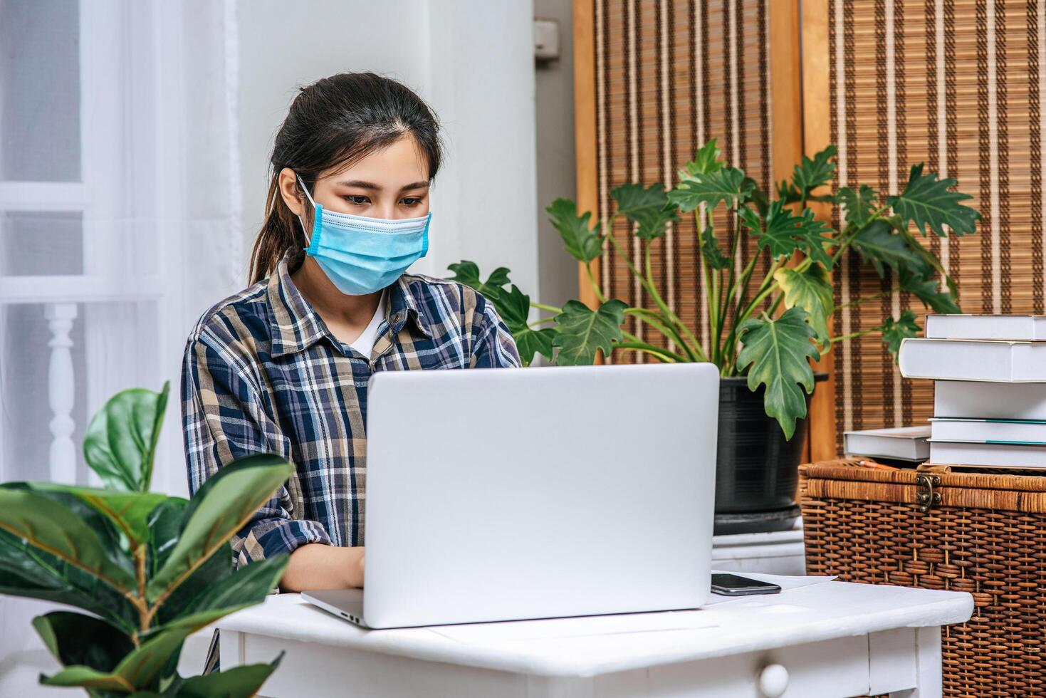 A woman wearing a mask uses a laptop to work. photo
