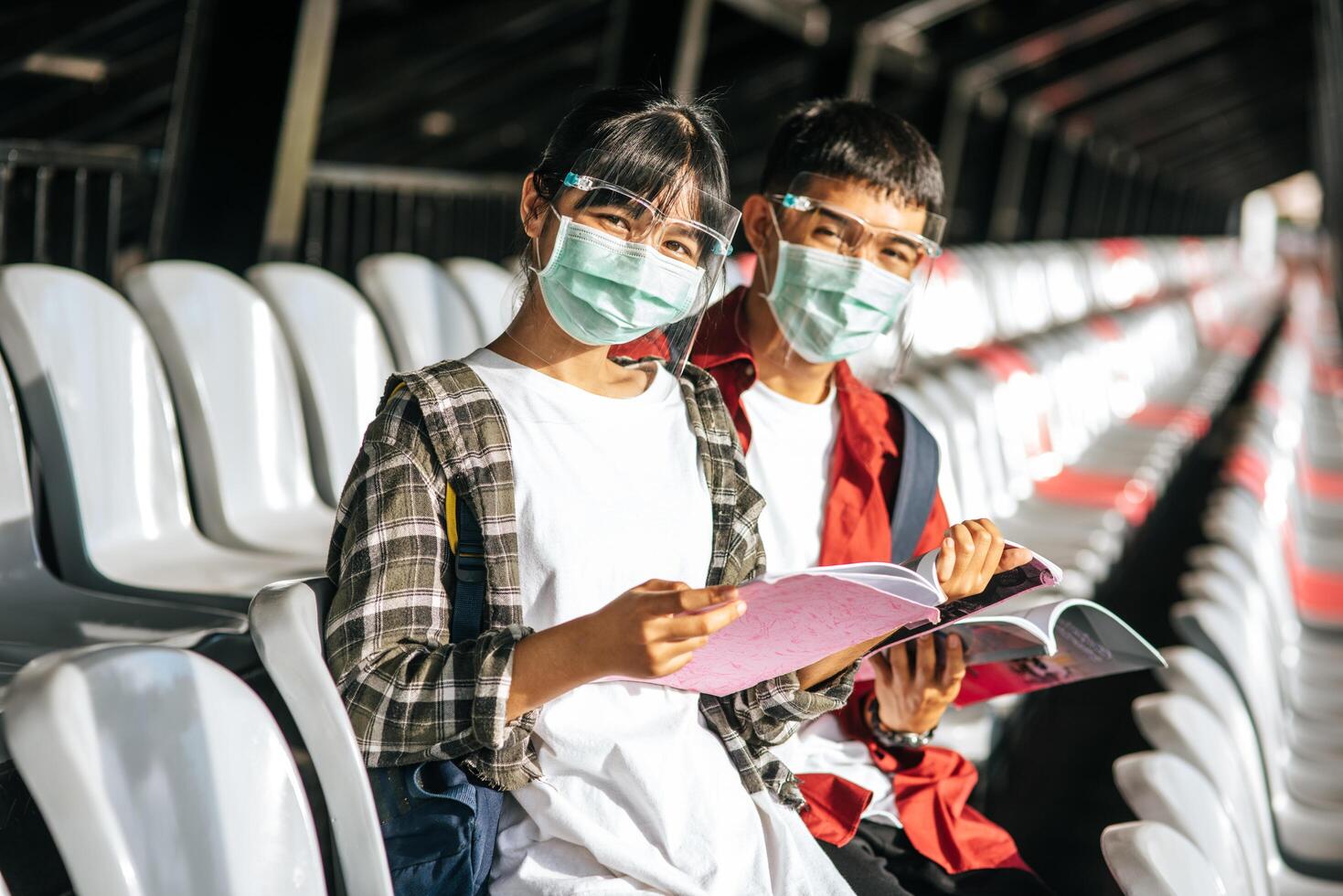 Male and female students wear masks and sit and read on the field chair photo