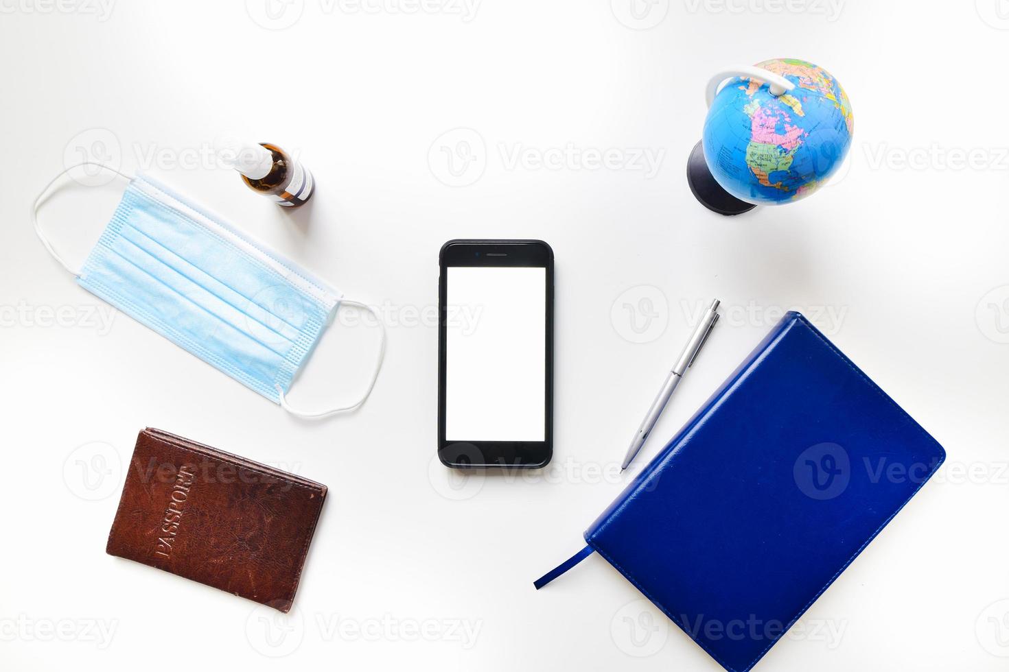 Top view flat lay mobile phone green screen copypaste with blue notebook, passport, sanitizer, blue face mask, global stand on white table isolated background. photo