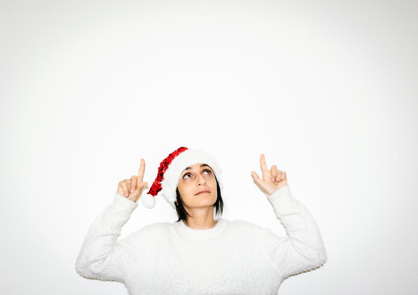 Mujer en ropa blanca de Navidad señala con el dedo hasta el fondo blanco del espacio en blanco.concepto de saludos estacionales y publicitarios. foto