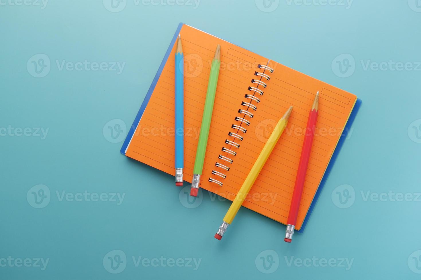 Close up of colorful pencils on notepad on light green background photo