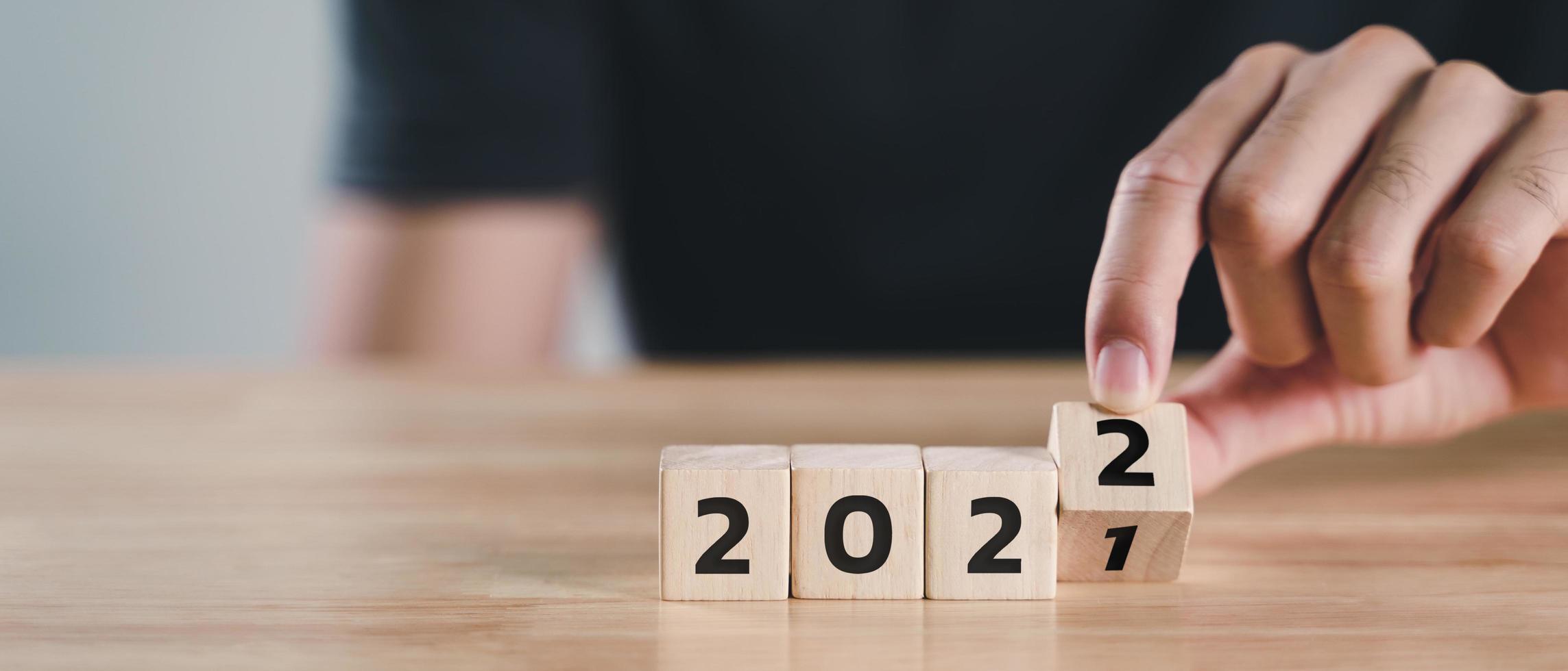 La mano del hombre voltea el bloque de cubo de madera para cambiar el año 2021 al año 2022 en la mesa de madera con espacio de copia. comienzo del año 2022. feliz año nuevo concepto. foto