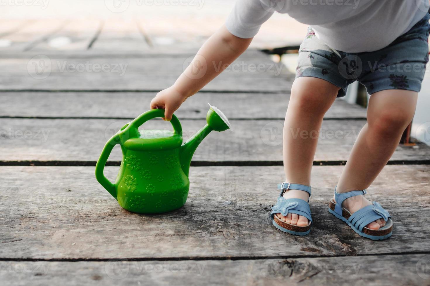 una niña pequeña está jugando con una regadera de un puente de madera. primavera y verano. jardinería. regadera verde foto