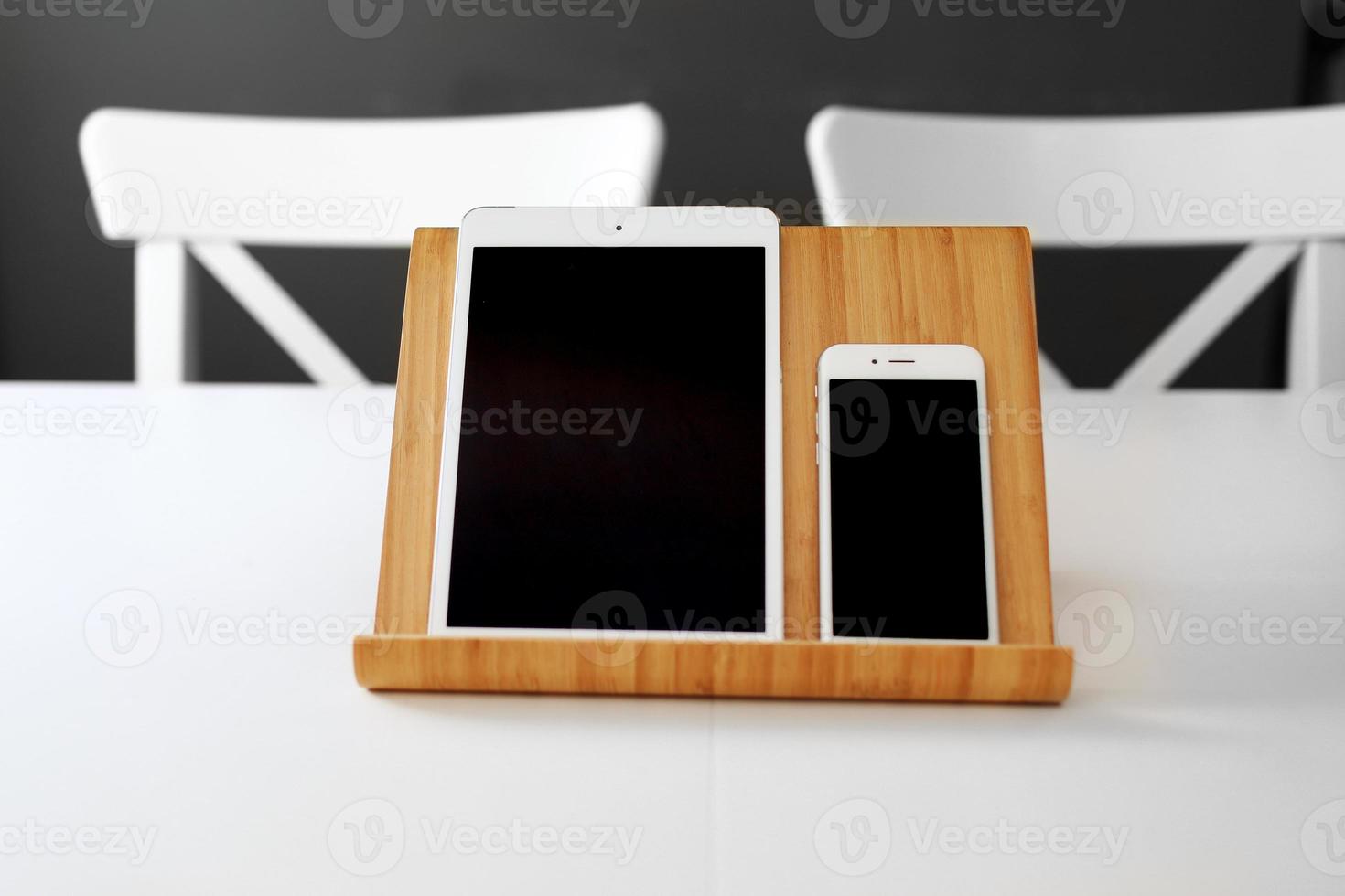 a white tablet and a smartphone with a black screen on a stand on a white table. office workplace photo
