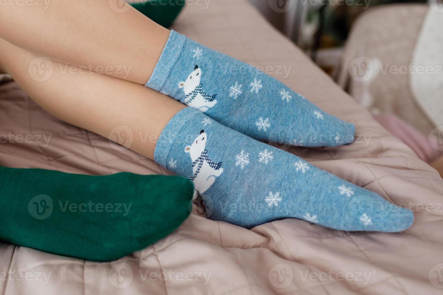 Legs with cute blue socks with white bears and green socks on the bed. Colored socks photo