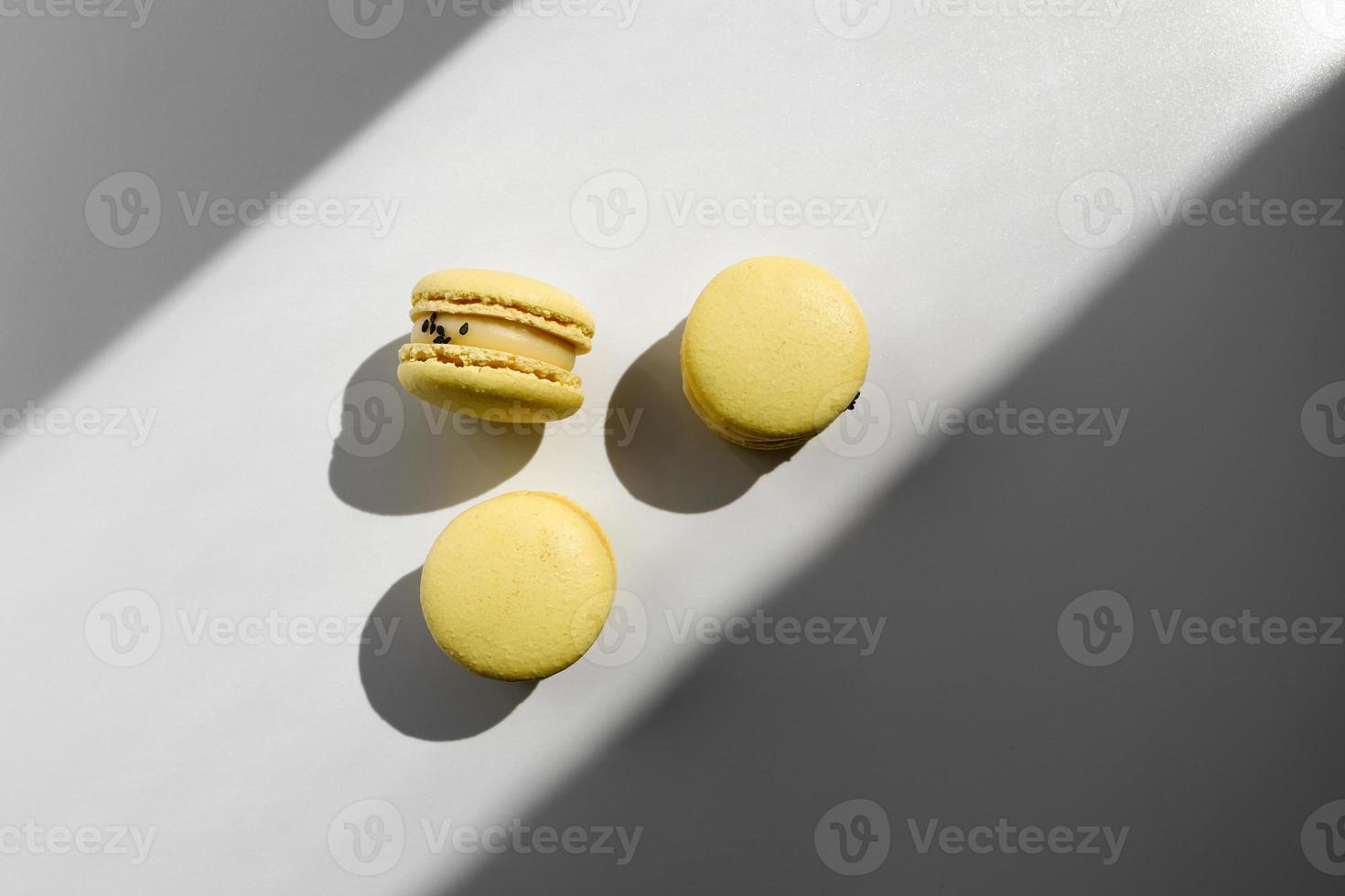 Tres dulces macarrones o macarons franceses de limón amarillo postre aislado sobre fondo blanco con rayos de luz desde la ventana foto