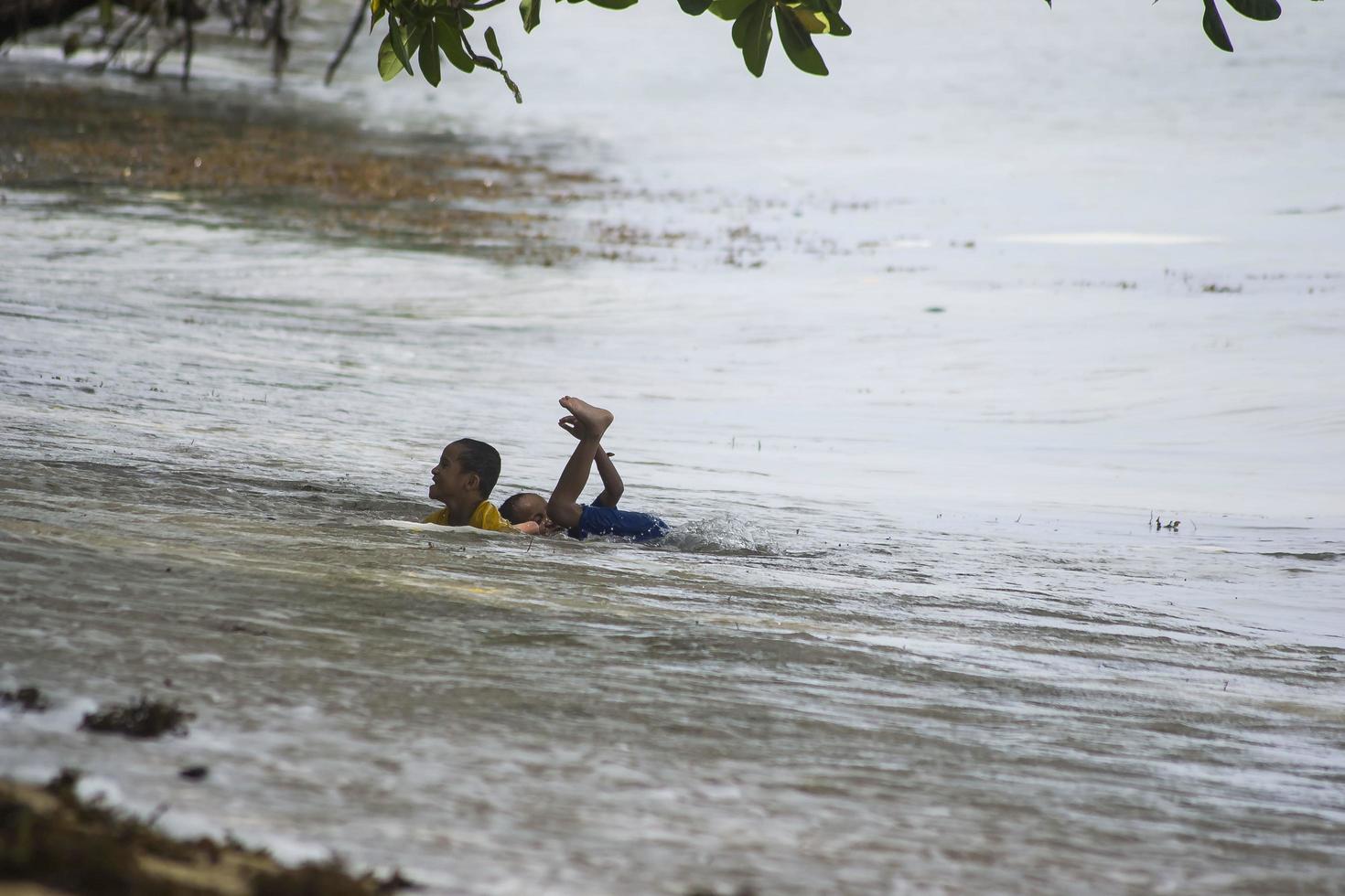 Sorong, West Papua, Indonesia, December 12th 2021. Boys playing against the waves on the beach photo