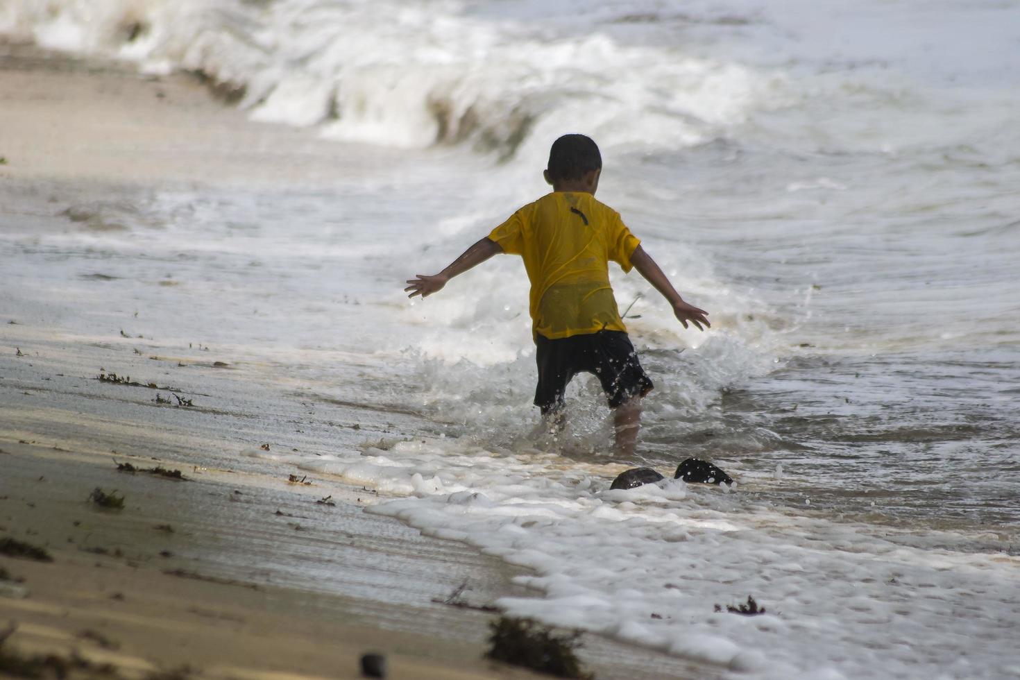 Sorong, Papua Occidental, Indonesia, 12 de diciembre de 2021. Niños jugando contra las olas en la playa foto