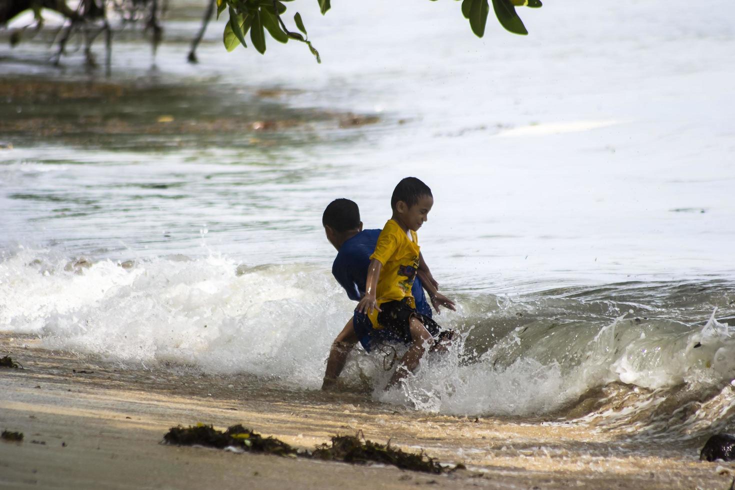 Sorong, West Papua, Indonesia, December 12th 2021. Boys playing against the waves on the beach photo