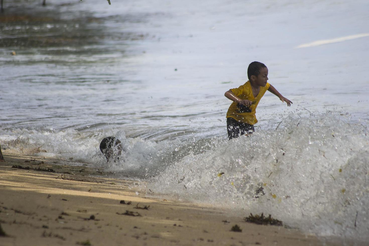 Sorong, West Papua, Indonesia, December 12th 2021. Boys playing against the waves on the beach photo