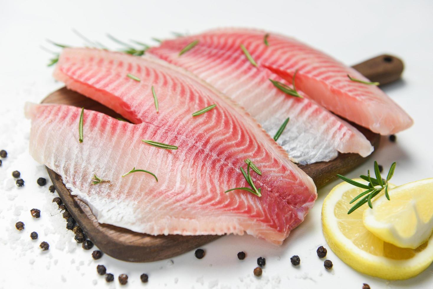 filete de pescado fresco en rodajas para bistec o ensalada con hierbas especias romero y limón - filete de tilapia crudo pescado y sal sobre fondo de piedra blanca e ingredientes para cocinar alimentos foto