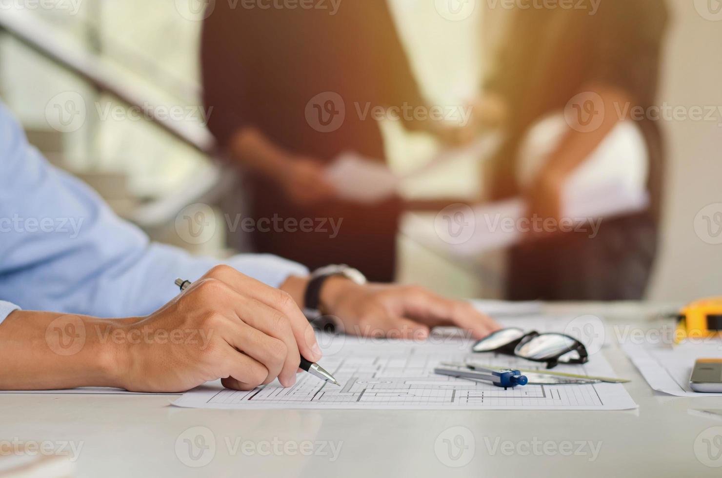 Close-up of an engineer planning a hand drawn design. with architect equipment architect at the table And there are subordinates who are talking in the background. Teamwork and workflow concepts photo