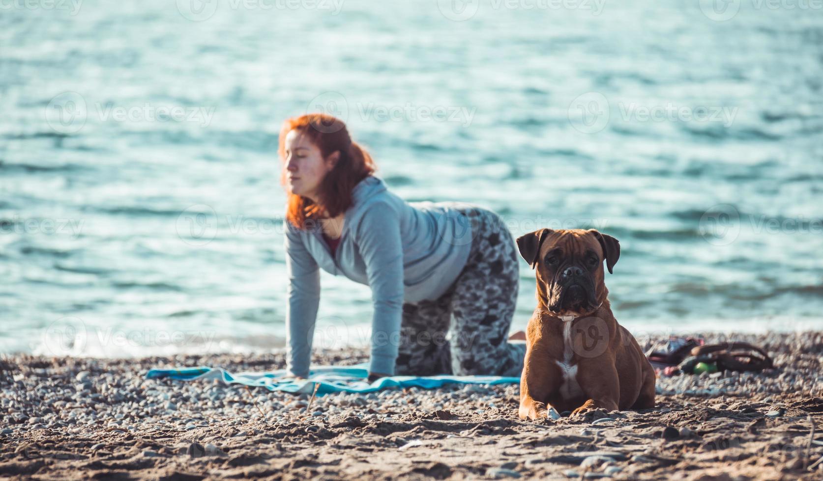 Mujer joven haciendo yoga y estiramientos en la playa con su perro foto