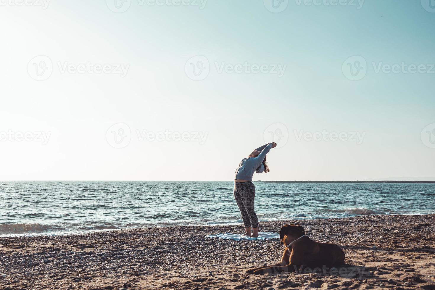 young woman doing yoga and stretching on the beach with her dog photo