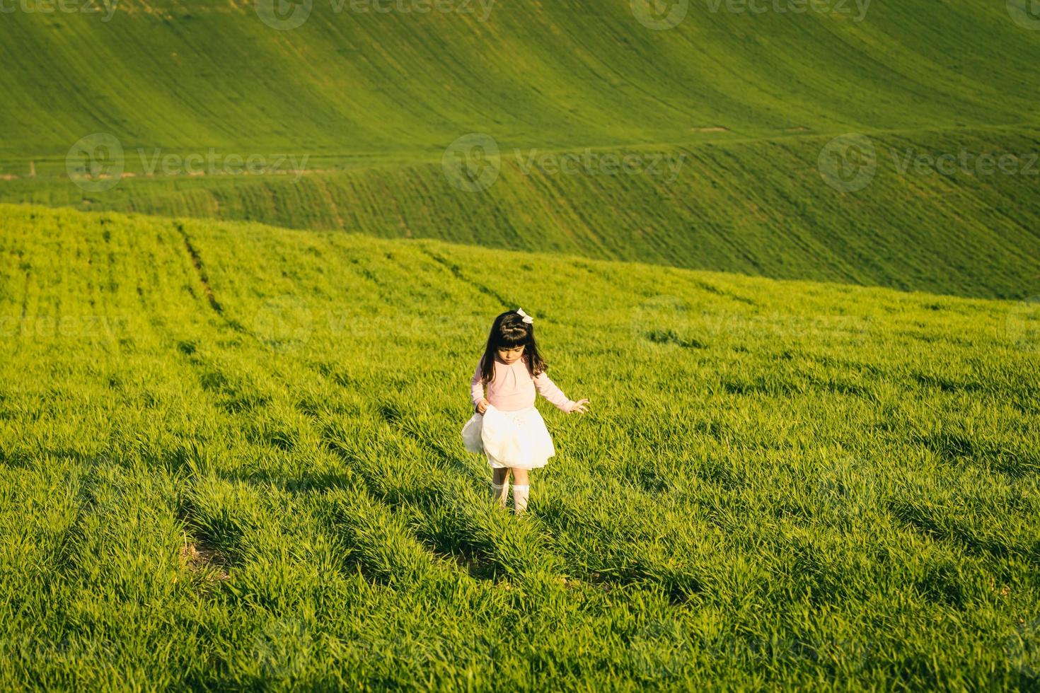 niña con camisa rosa y falda en un prado. cara de disgusto. a ella no le gusta el campo foto