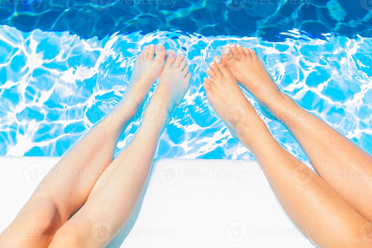 Young girls sit on the edge of swimming pool and chat with their feet in the water photo