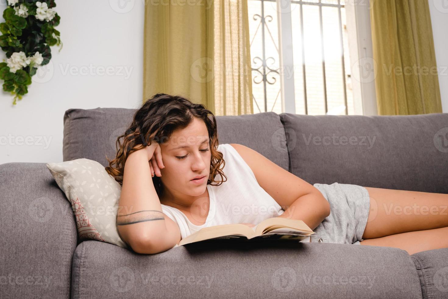 woman reading a book in the living room sitting on the couch photo