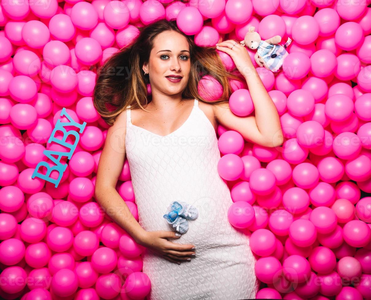 Young pregnant woman playing in a pink ball pool photo