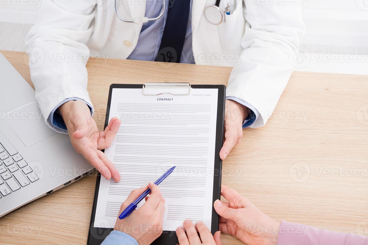 Doctor and patient are discussing something, hands at the table. Medical insurance. Doc sitting in cabinet. Man in white uniform. photo