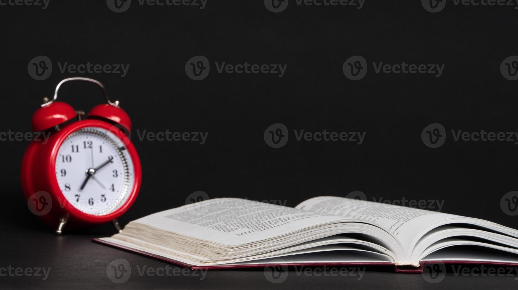 red alarm clock and open book on black background, isolated. back to school photo