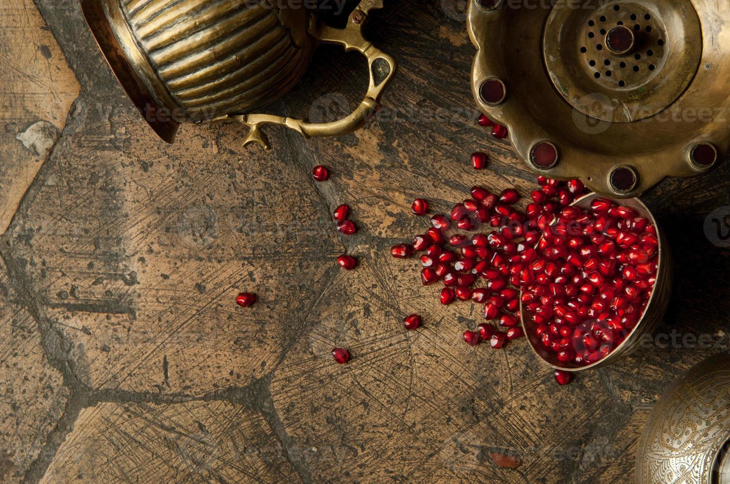 grains and seeds of pomegranate with a copper jug on an old decorative paving stone. antique copper jug with a pomegranate on an old tile photo