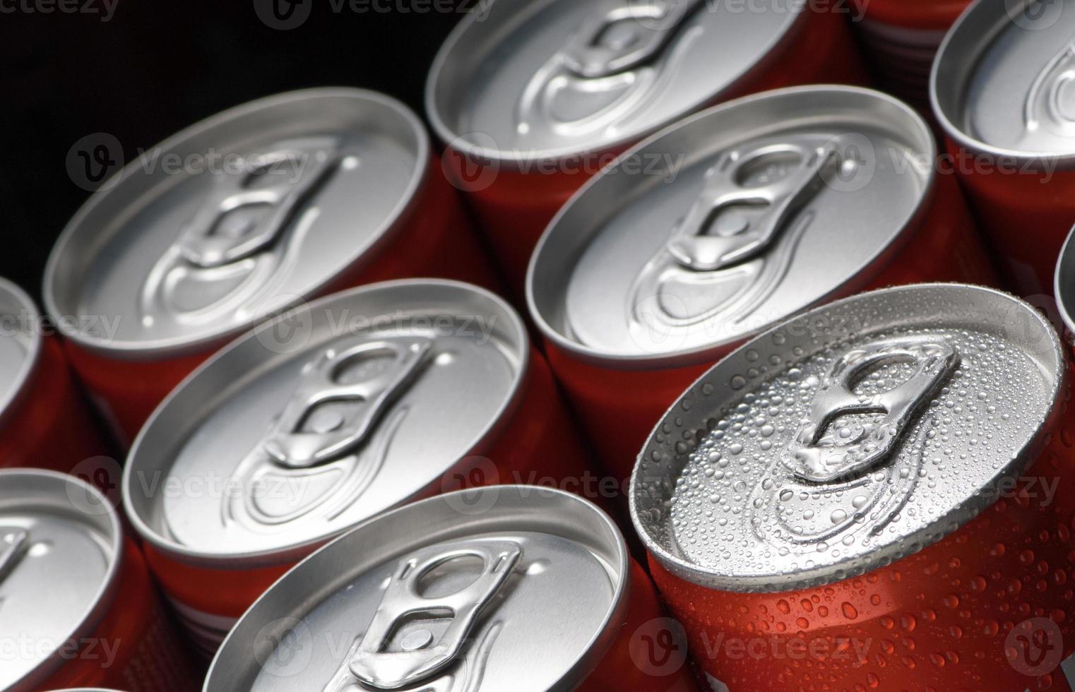 Un grupo de latas rojas con gotas de agua de cerca sobre un fondo negro foto