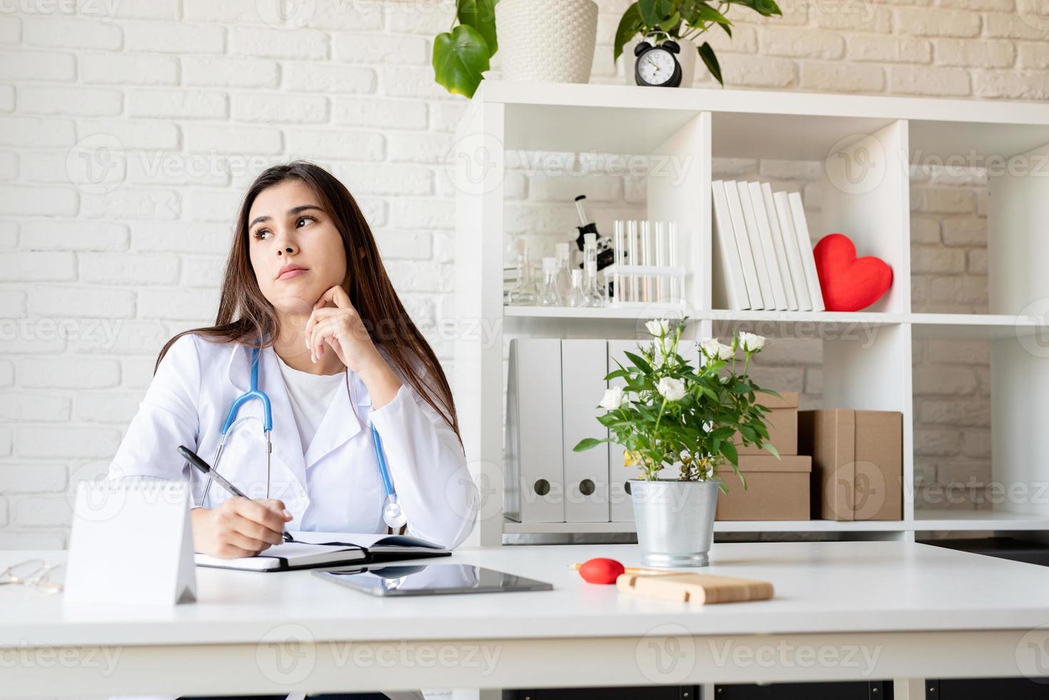 Young doctor woman writing in her cabinet filling medical history or anamnesis photo