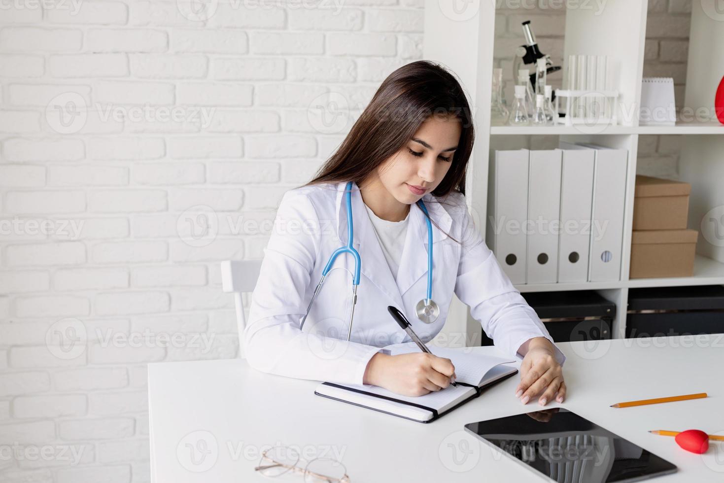 Young doctor woman writing in her cabinet filling medical history or anamnesis photo