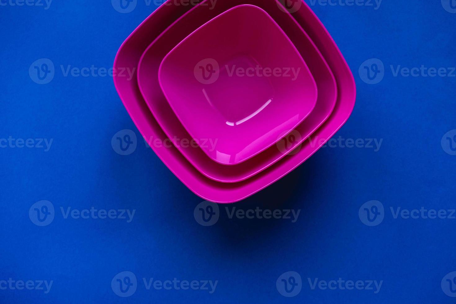 Set of pink plates on blue background. Plastic utensils for the kitchen photo