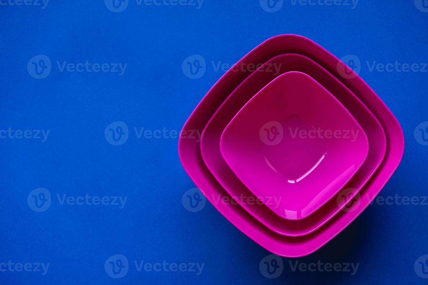 Set of pink plates on blue background. Plastic utensils for the kitchen photo