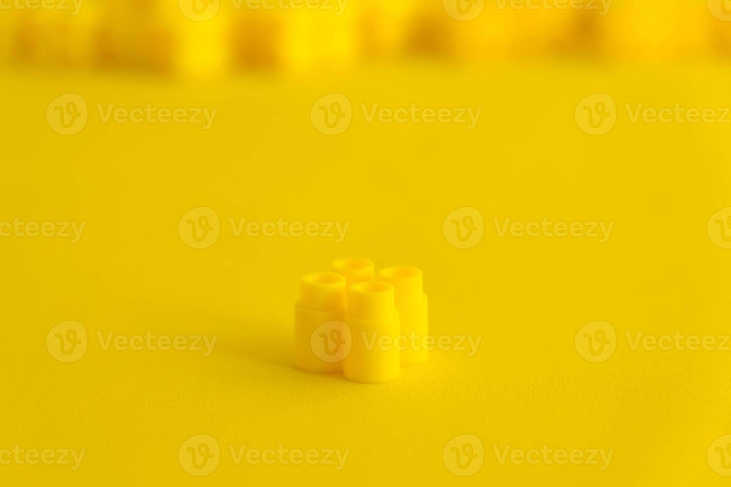 Yellow plastic building block on yellow background photo