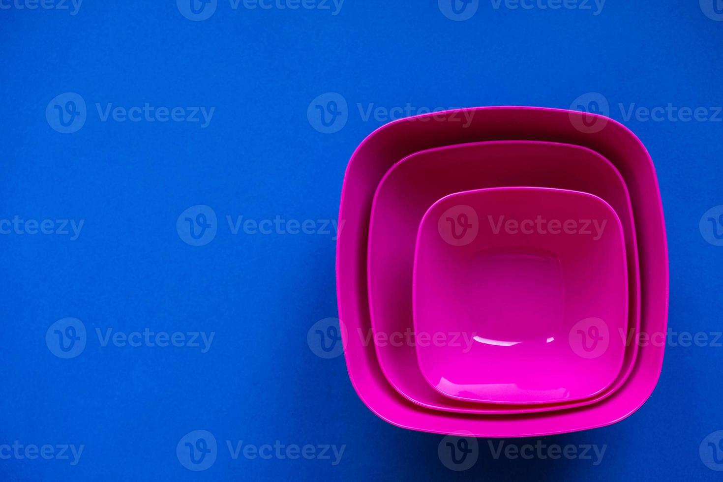 Set of pink plates on blue background. Plastic utensils for the kitchen photo
