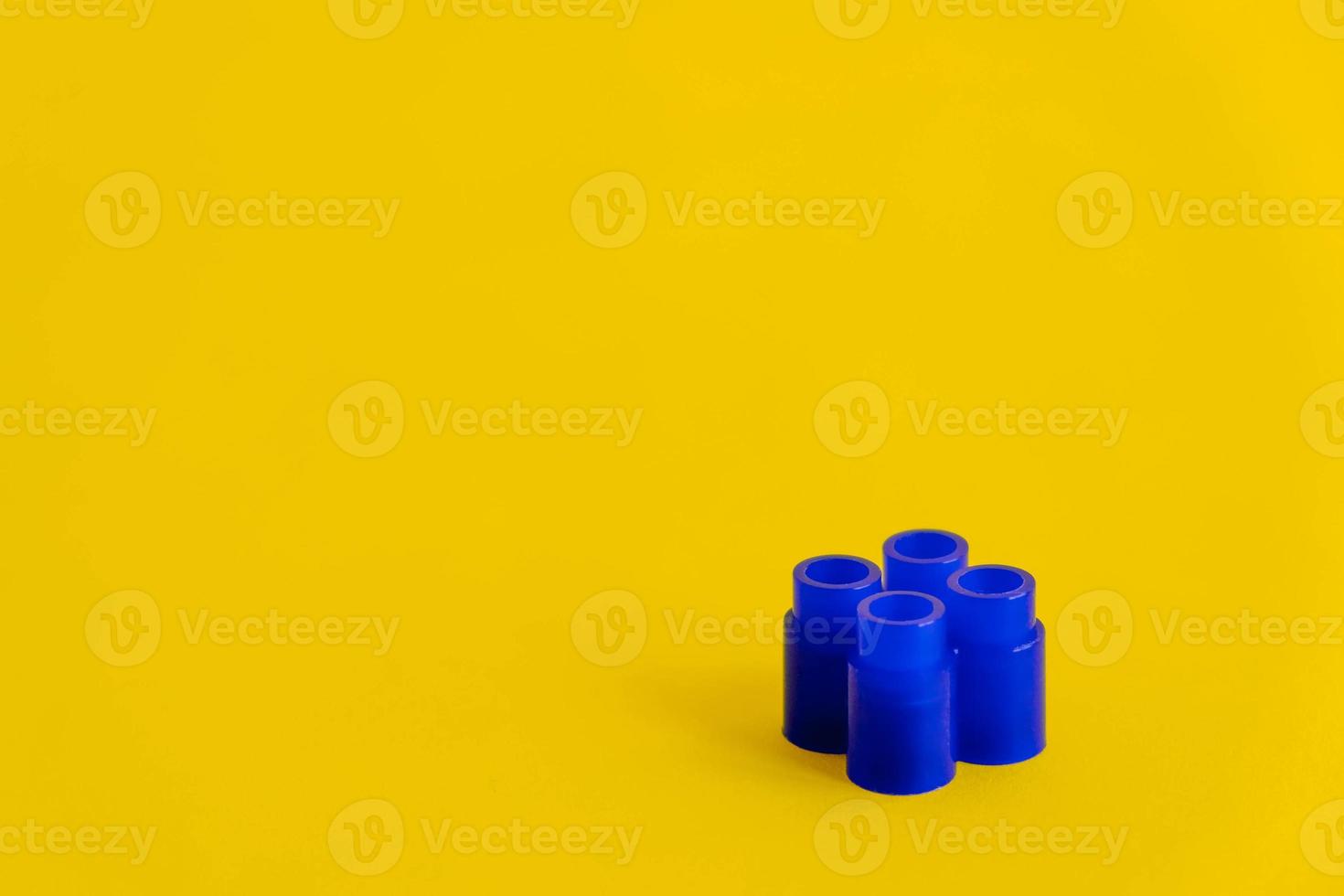 Blue plastic building block on yellow background. Background of plastic detail building block. Part of bright small spare part for toys photo