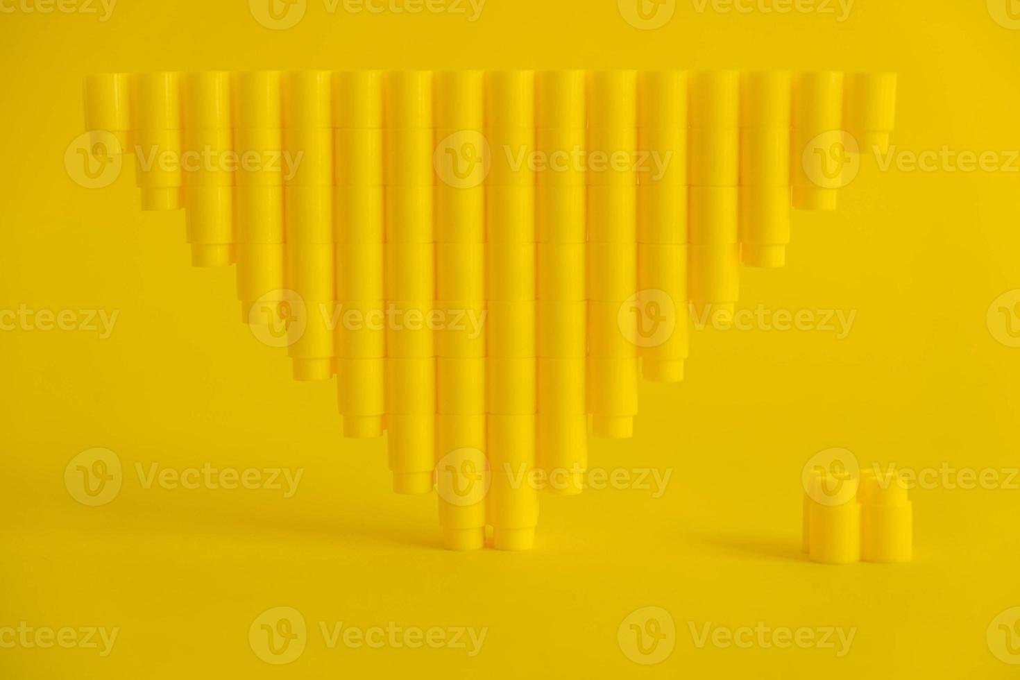 Yellow plastic building blocks in shape of a pyramid on yellow background photo