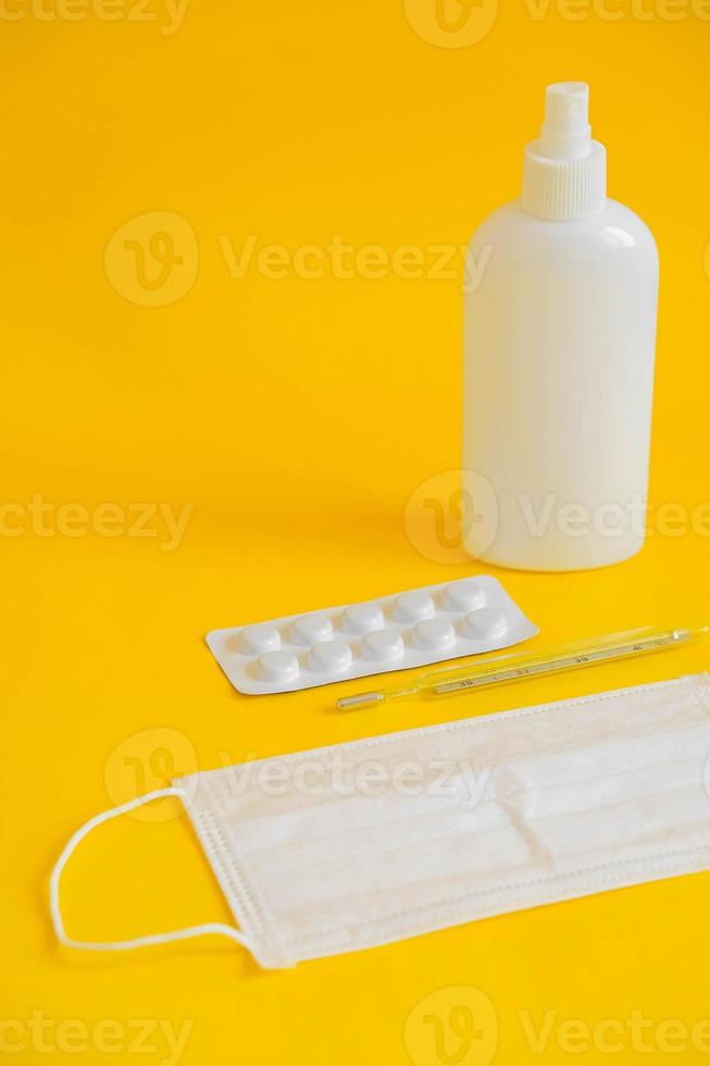 conjunto de mascarilla médica desechable, antiséptico, pastillas y un termómetro de mercurio sobre un fondo amarillo. concepto de higiene médica y protección antivirus foto