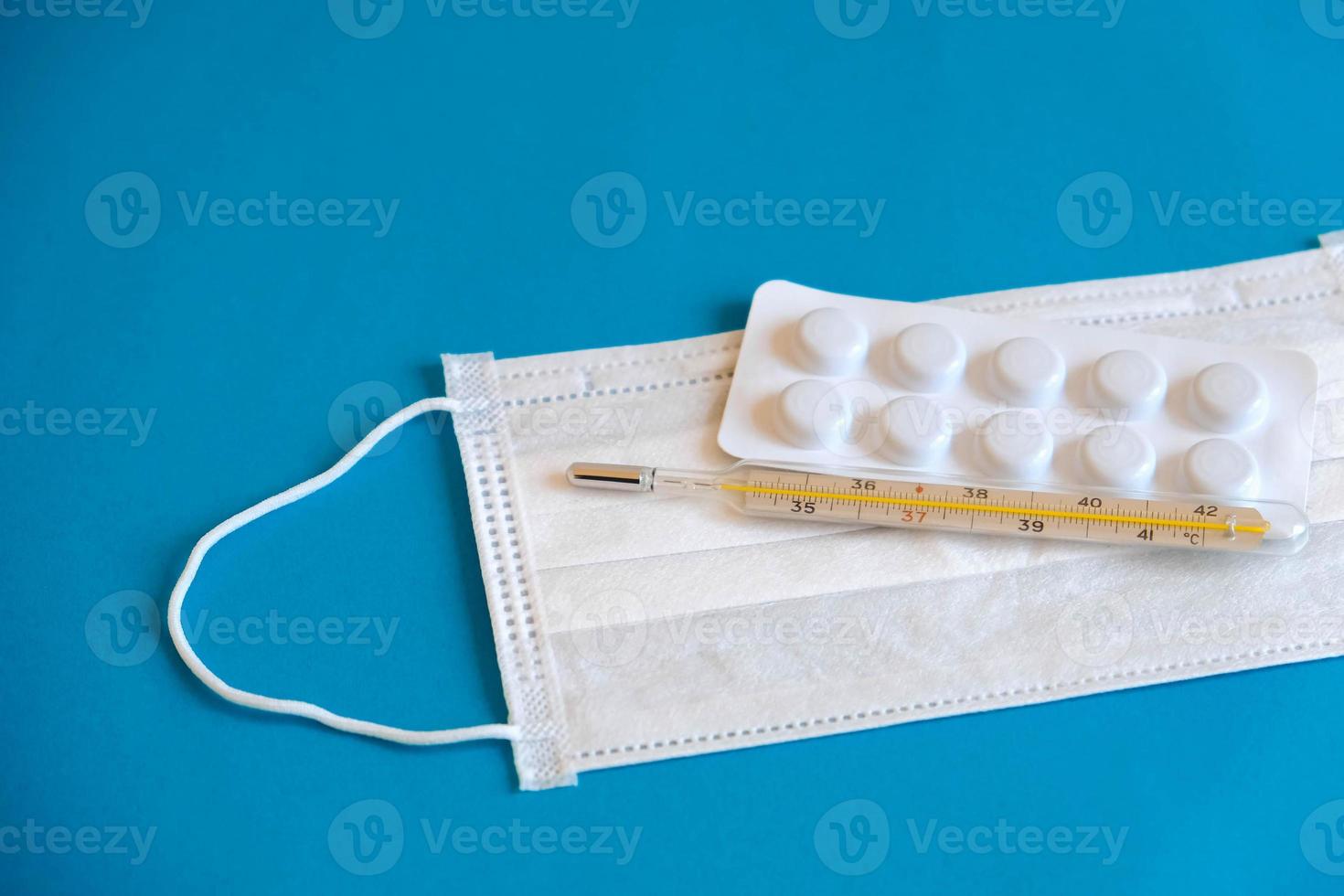 Medical disposable mask, pills and a mercury thermometer on a blue background photo