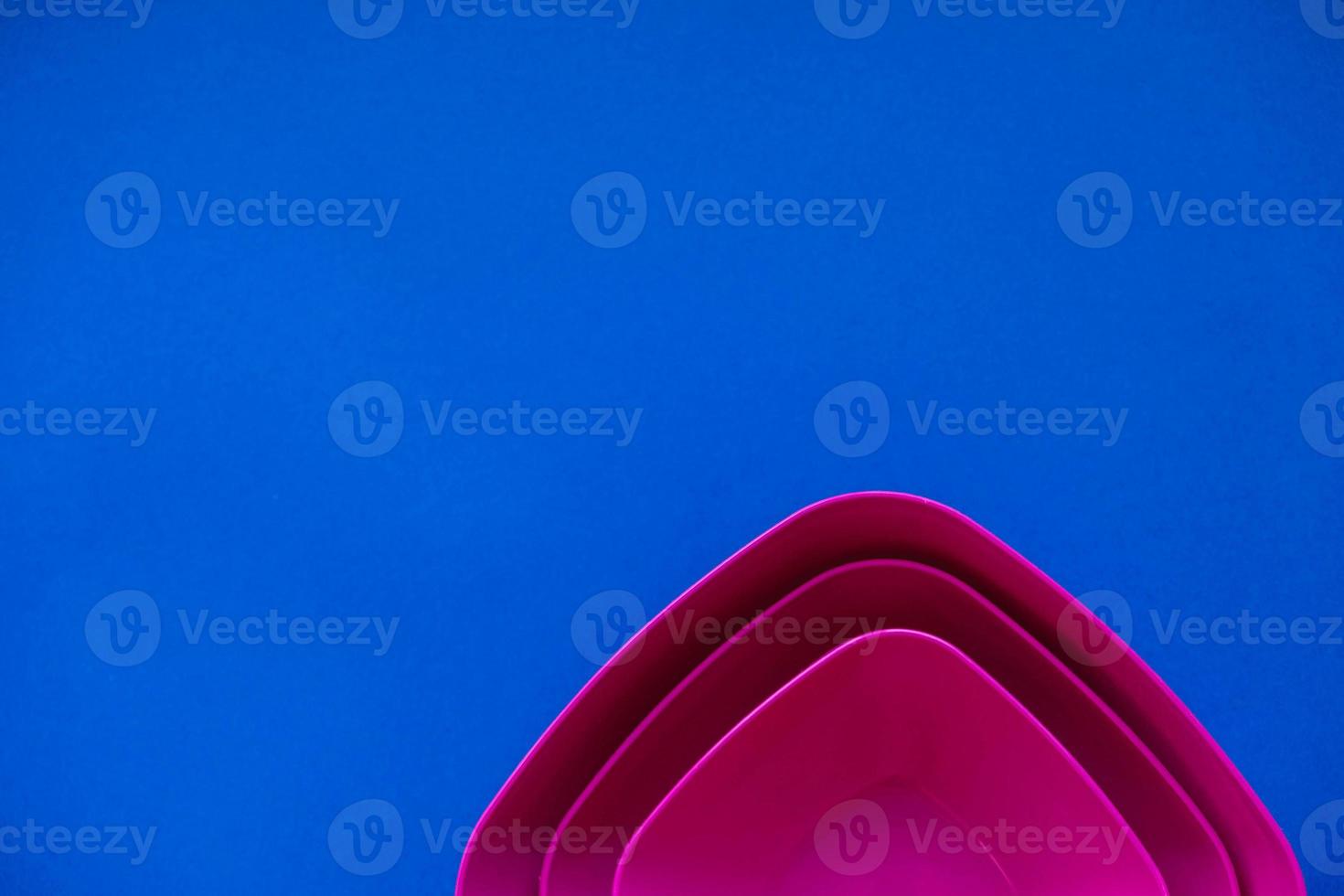 Set of pink plates on blue background. Plastic utensils for the kitchen photo