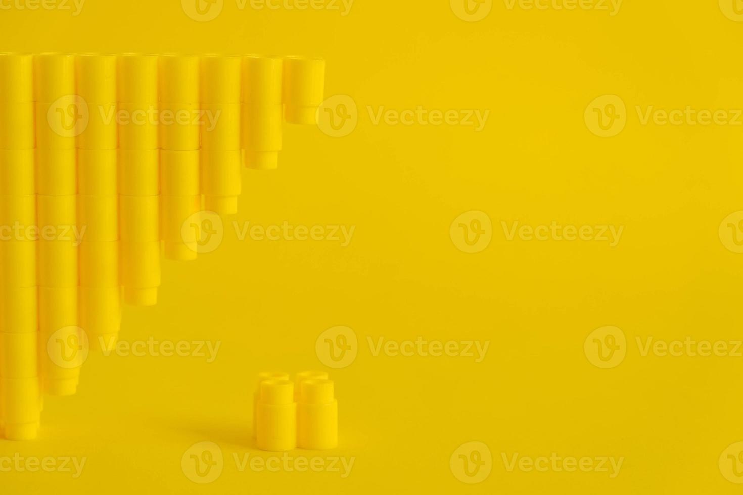 Yellow plastic building blocks in shape of a pyramid on yellow background photo
